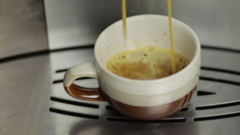 espresso disparado saliendo de la máquina de café en una pequeña taza blanca y marrón.