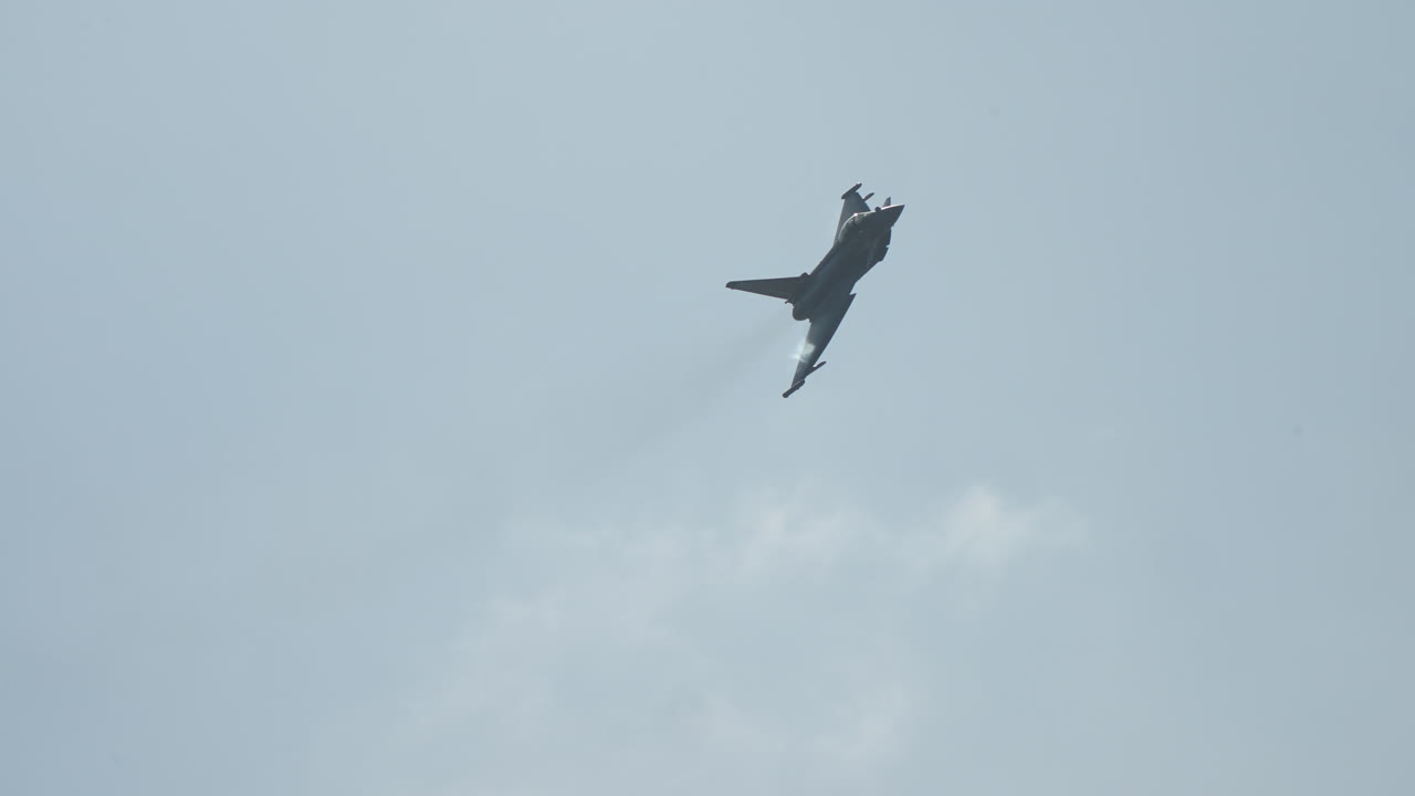 Military jet fighter in flight performing a steep aerial maneuver against a clear sky