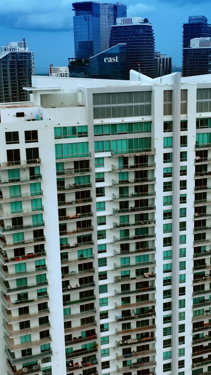 Descending above the high-rise buildings in Miami, Florida, USA. Waterscape under dark blue sky at backdrop. Vertical video