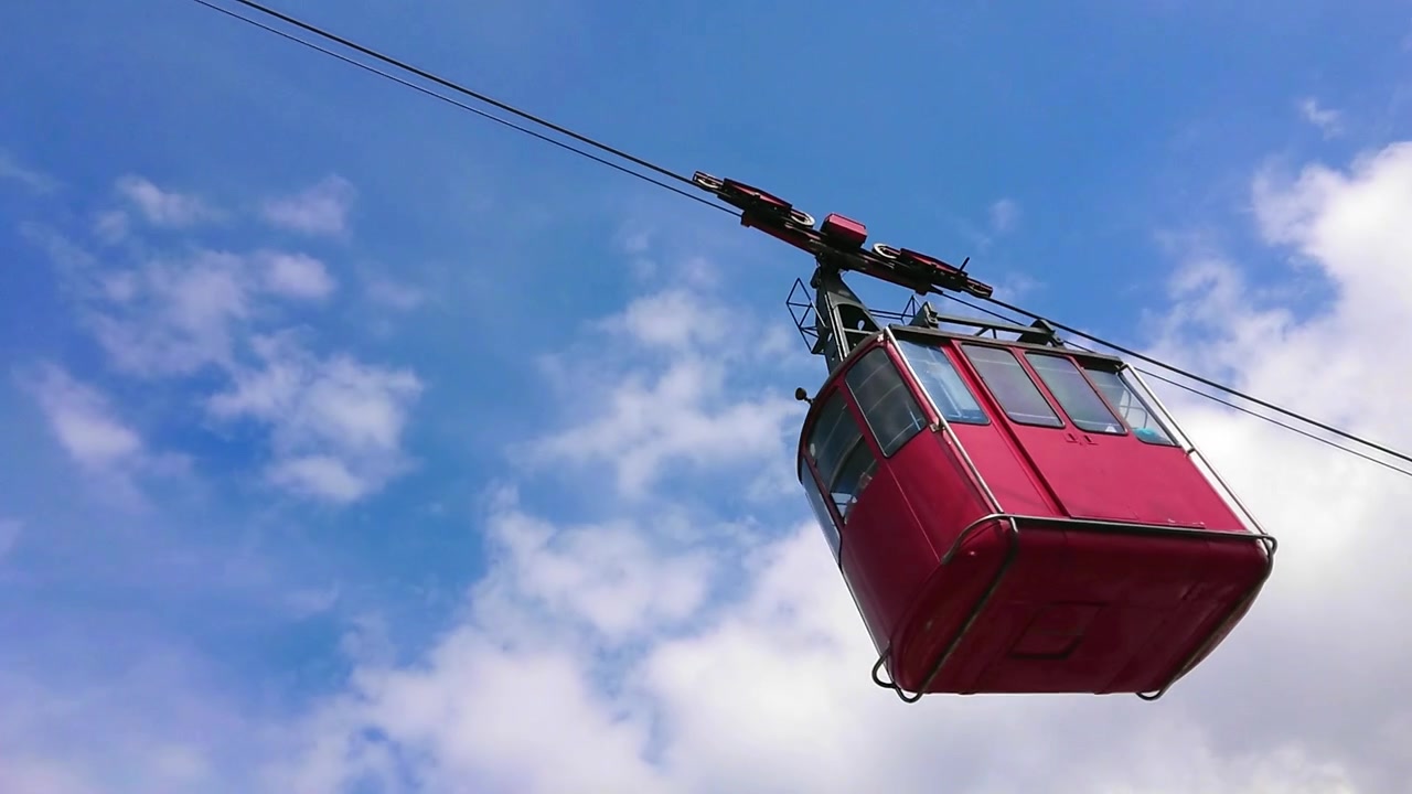 Teleférico vermelho subindo a montanha em um dia ensolarado de verão.