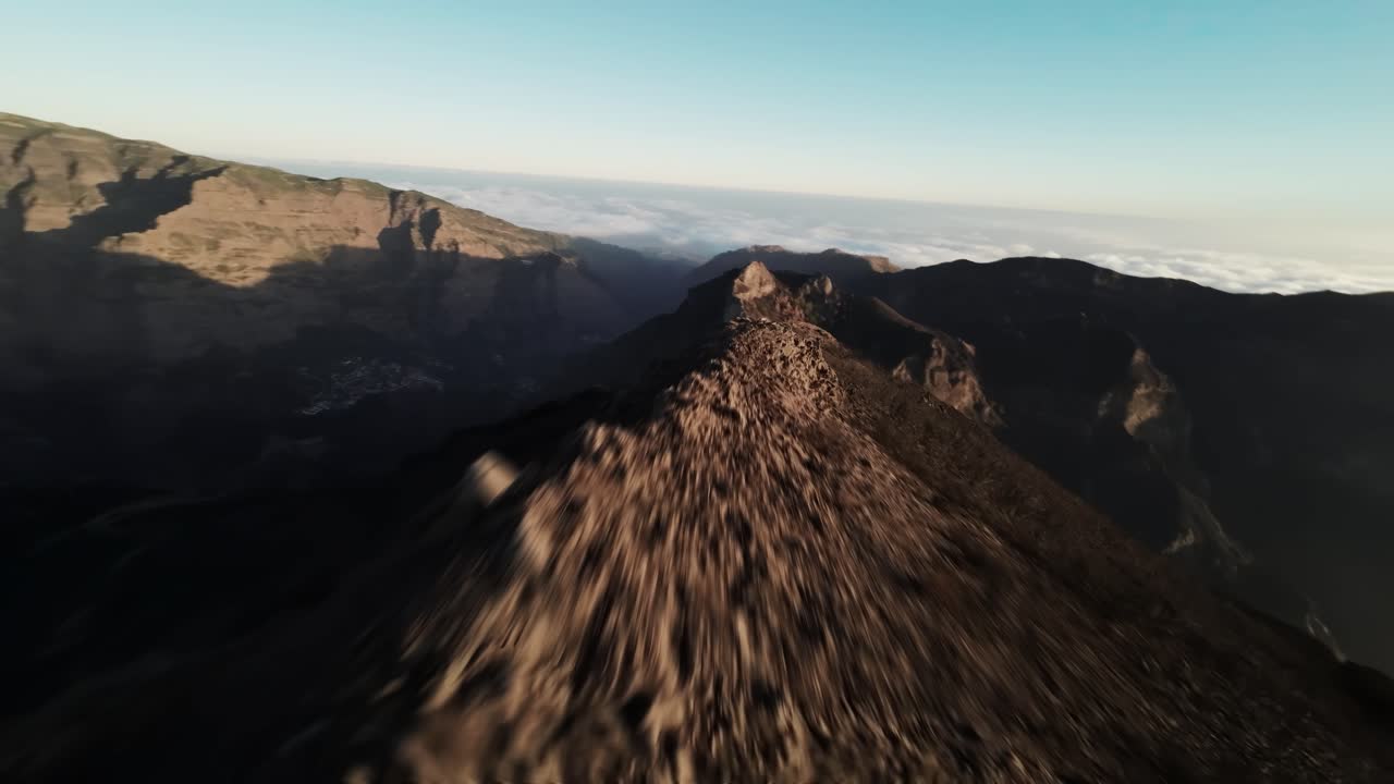 FPV aerial tracking along a jagged ridgeline at Pico do Arieiro, Madeira, with golden morning light and cloud horizon