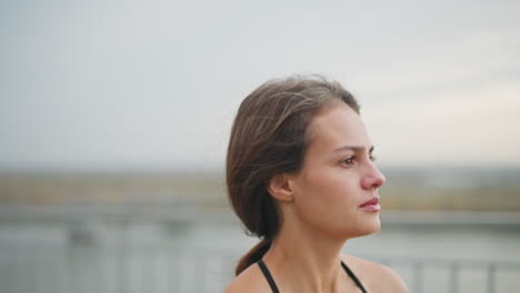 closeup view of a determined woman running outdoors, showcasing her focused expression while her hair flows back as she jogs near a river with an iron fence in the background