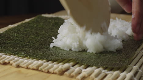 rice being spread over seaweed to make sushi roll