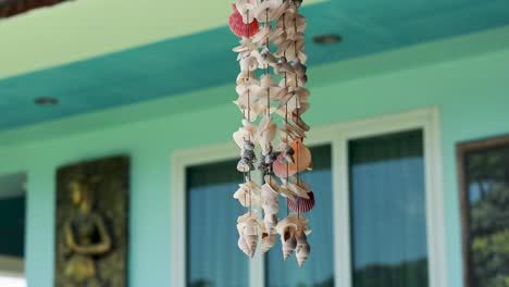 a shell wind chime gently sways in the breeze outside a colorful building in phuket, thailand, under soft daylight