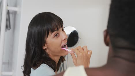 happy diverse couple looking in mirror and brushing teeth in bathroom