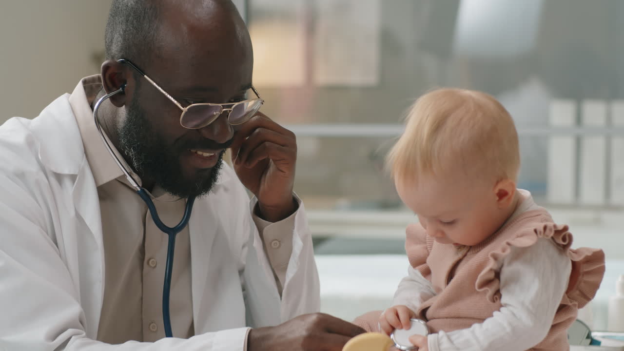 Black Pediatrician Using Stethoscope and Giving Checkup to Caucasian Baby