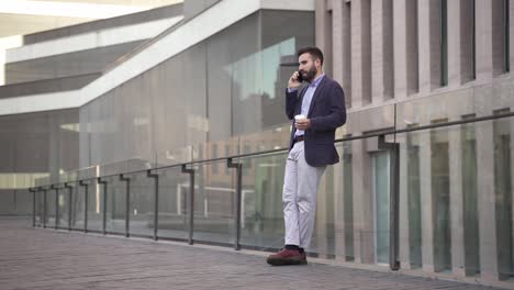 young middle east businessman talking on phone in a modern corporate business district. casual young arab professional executive in the city
