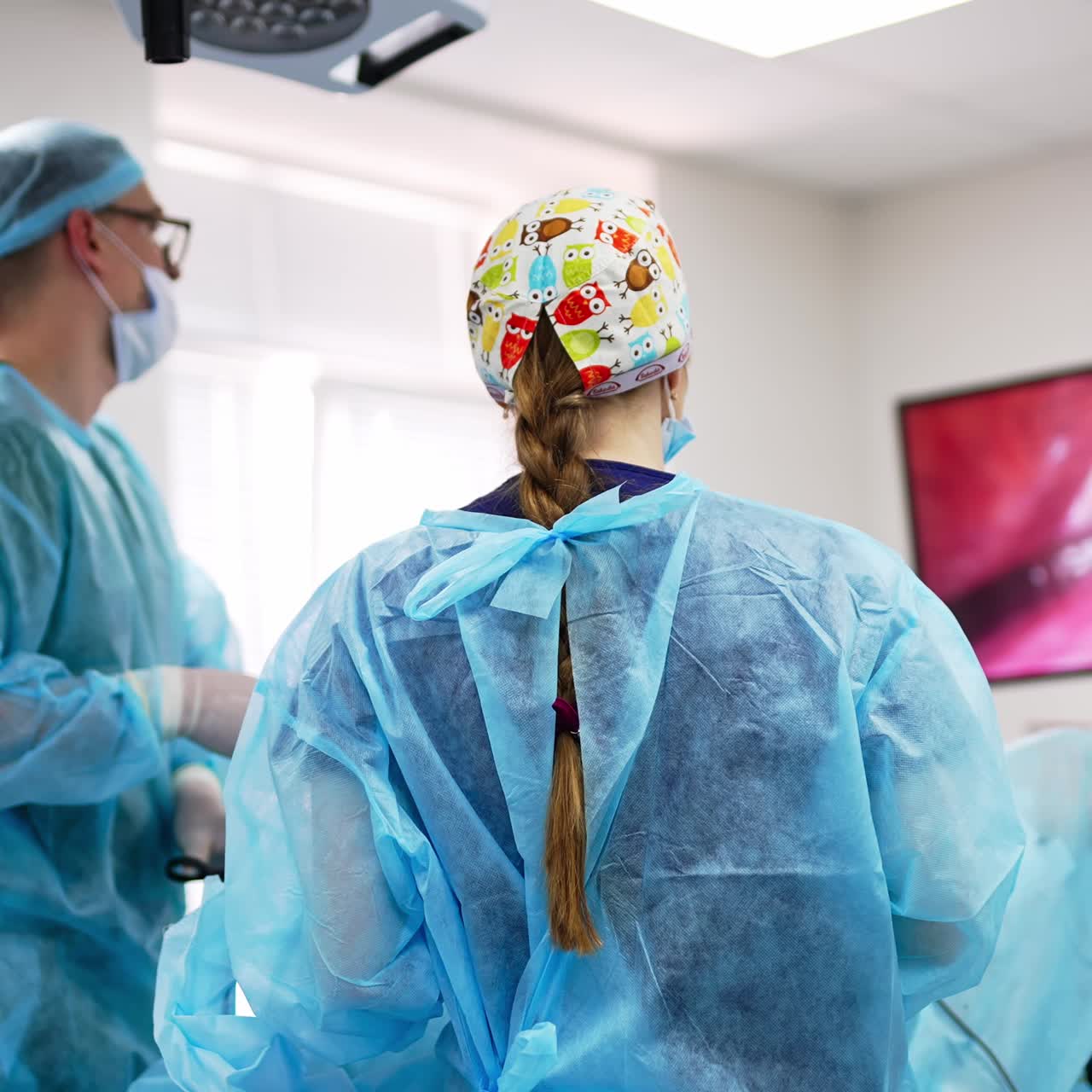 Medical colleagues stand in the surgery room looking at the screen. Surgeon carefully moving instruments watching the monitor