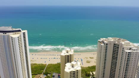 Aerial-drone-shot-slowly-flying-over-the-Ritz-Carlton-and-other-residential-buildings-toward-the-Atlantic-Ocean-with-waves-crashing-on-the-sandy-beach-and-clouds-slowly-moving-across-blue-skies