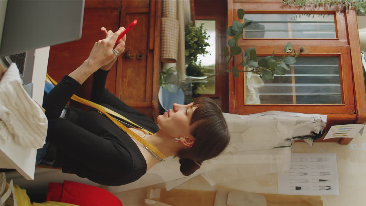 작업실에서 스마트폰을 사용하는 여성 의상 제작자