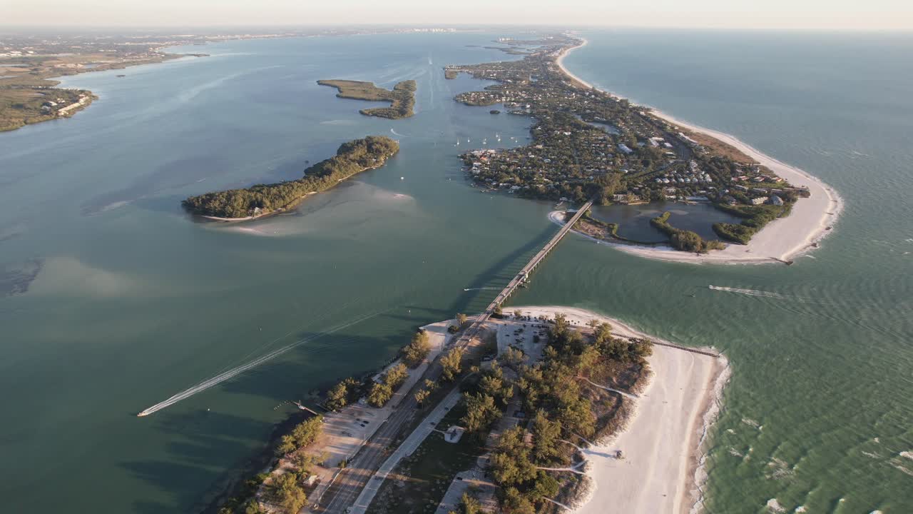 넓은 드론 클립은 수평선을 향해 열린 바다와 도로 다리로 연결된 긴 숲이 있는  ⁇  모래 해변 섬을 보여줍니다.