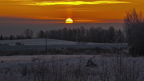 Malerische-Zeitrafferaufnahme-Des-Sonnenaufgangs-über-Dem-Gelben-Himmel-Und-Fliegender-Wolken-über-Einem-Verschneiten-Feld-Entlang-Einer-Straße-Mit-Vorbeifahrenden-Autos