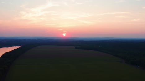 hermoso sol naranja rosa se asoma a través de las nubes y se refleja en el increíble río potomac en maryland rodeado de granjas, antena de drones