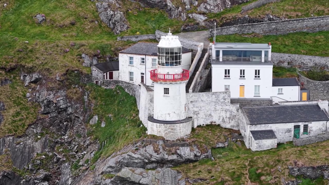 Filmatisk nærbilde fra luften av Gamle Wicklow Head fyr over ulendte klipper og Irskesjøen.