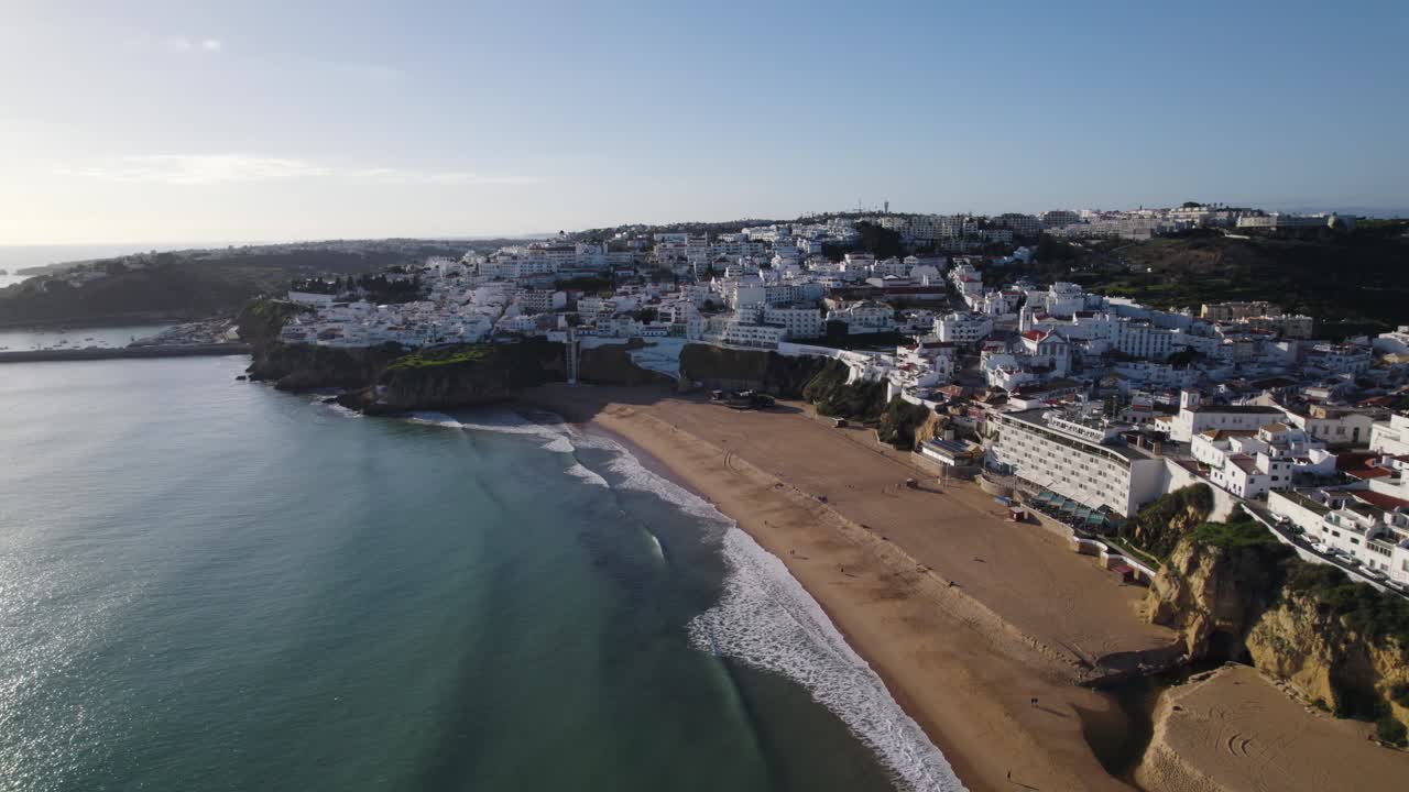 Panorama-Luftaufnahme eines breiten Sandstrandes mit sanften Wellen und weißen Apartmenthäusern in Albufeira, Portugal