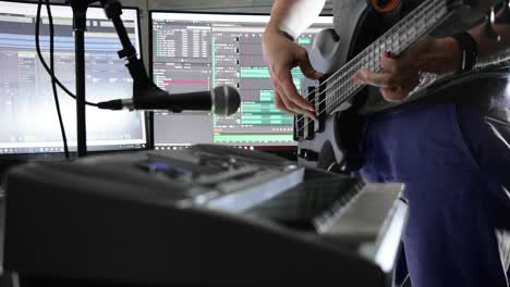 musician playing bass guitar in a home studio with pc screens displaying software