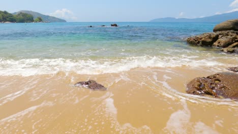 playa paradisíaca con olas azules rompiendo en la arena y rocas costeras