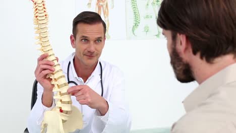 médico mostrando a su paciente un modelo de columna vertebral