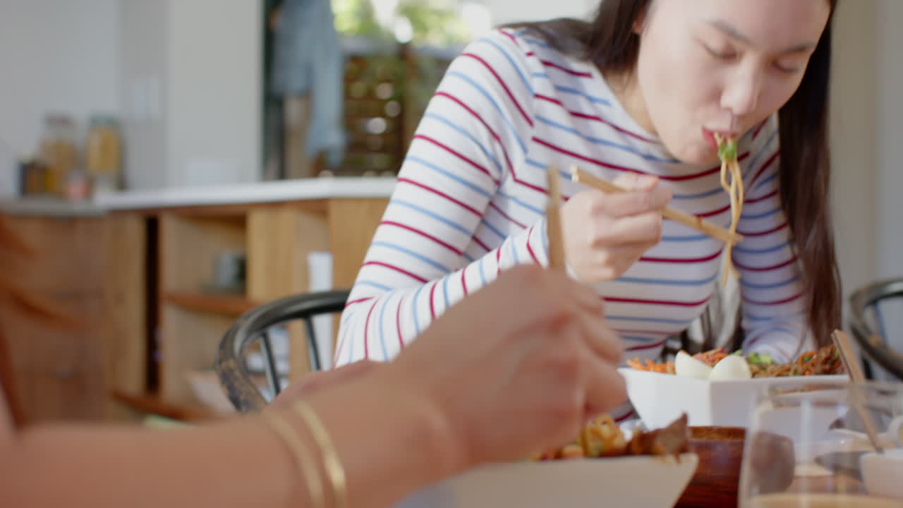 Eating noodles with chopsticks, asian mother and daughter enjoying meal together at dining table
