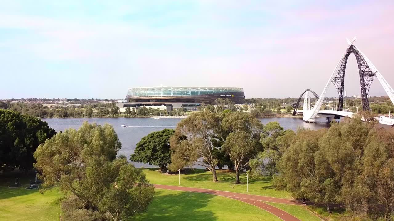 Aerial rise up view of Perth Stadium and the Matagarup pedestrian bridge over the Swan River