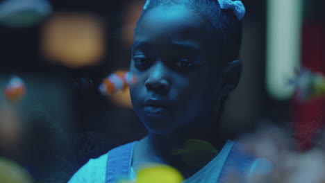 black girl looking at fish in aquarium curious child watching colorful sea life swimming in tank learning about marine animals in underwater ecosystem inquisitive kid at oceanarium