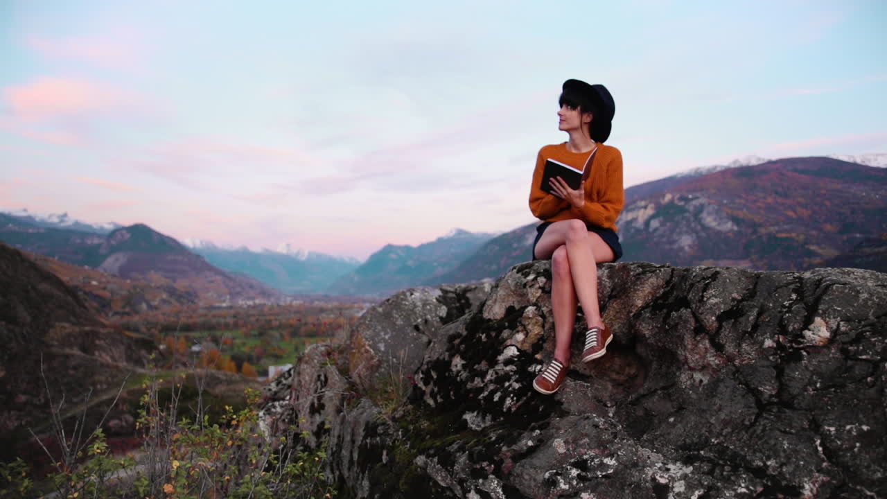 Young woman sitting on a rock in an alpine environment, writes in her notbeook