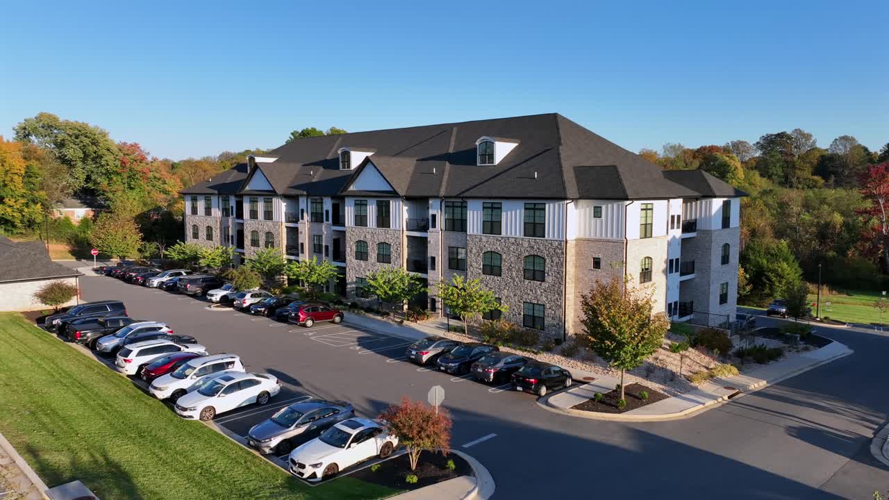 Luxury apartment of West Edge in Lynchburg, Virginia. Sunny day in fall season with many parking cars. Colorful foliage trees and blue sky at sunset. Modern architecture residential block. Aerial view