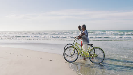 Pareja-Afroamericana-De-Alto-Rango-Caminando-Con-Bicicletas-En-La-Playa