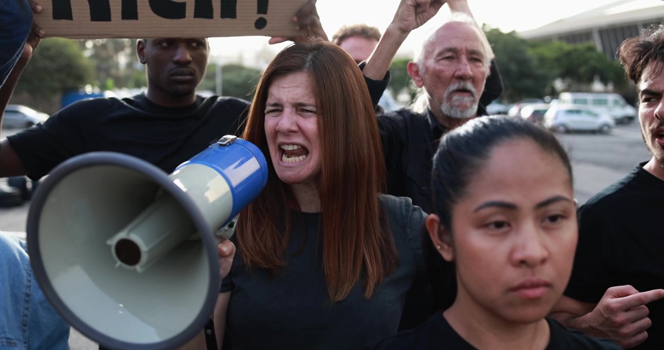 Donna che grida in un megafono a una manifestazione di protesta eterogenea.