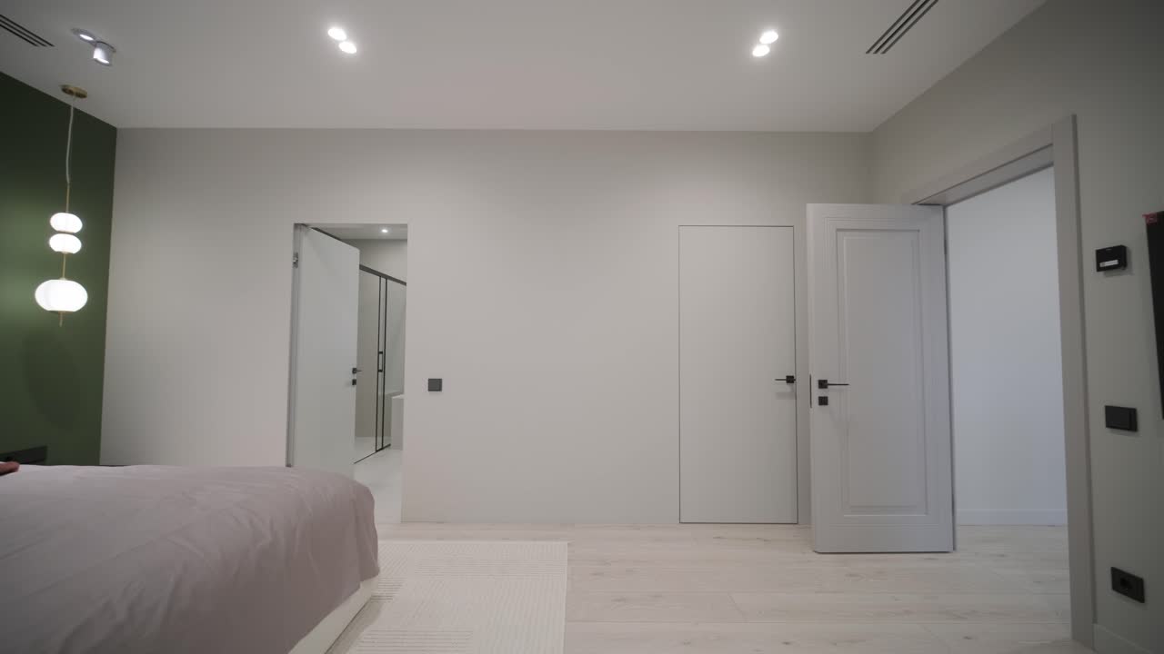 una escena de dormitorio serena con una cama de peluche adornada con un lanzamiento de color óxido, acentuada por una pared de característica verde oscuro y una vista a un baño luminoso, evocando una sensación de comodidad moderna