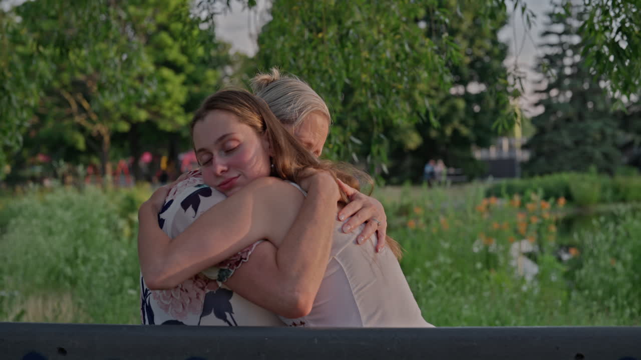 A Young Woman Hugs Her Mother Tightly In A Public Park, Surrounded By Lush Summer Nature. A Moment Of Deep Love, Trust, And Emotional Connection