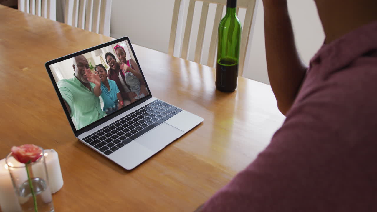Biracial man sitting at table using laptop making video call with family