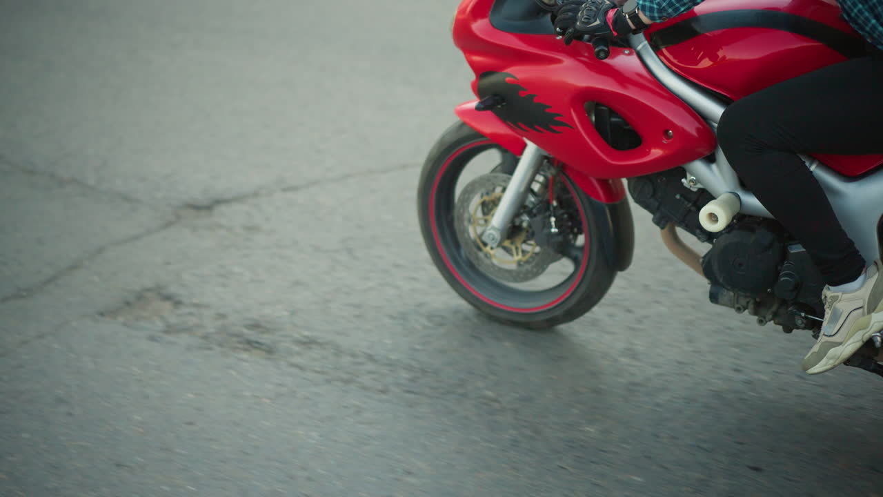 A lady rides a red power bike on a smooth tarred road with the wind raising her checkered shirt, partially exposing her midriff