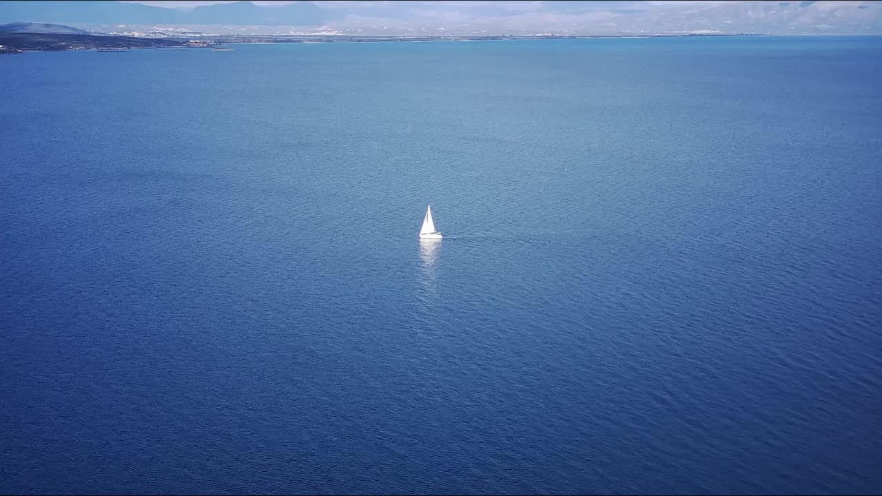 지평선에 산을 볼 수 있는 푸르키즈색 물 위에 있는  ⁇ 색 세일보트의 아름다운 영상
