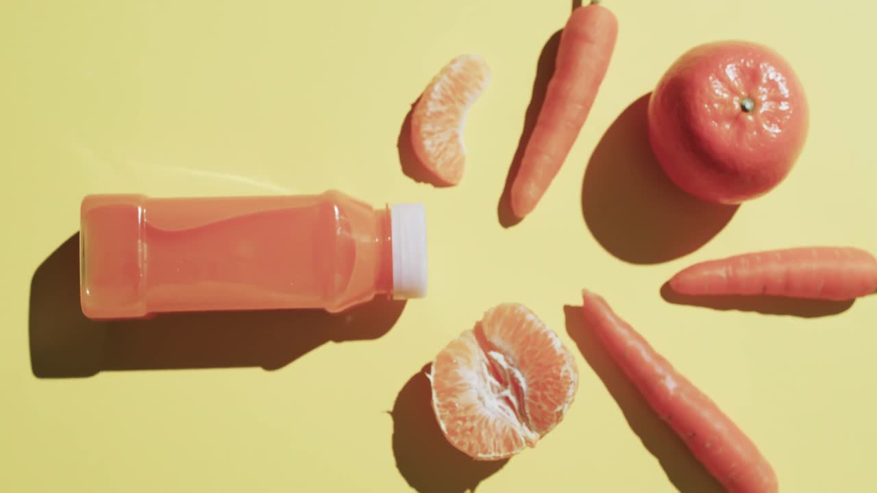 video de una botella de jugo de frutas, zanahorias y mandarinas con espacio de copia sobre fondo amarillo