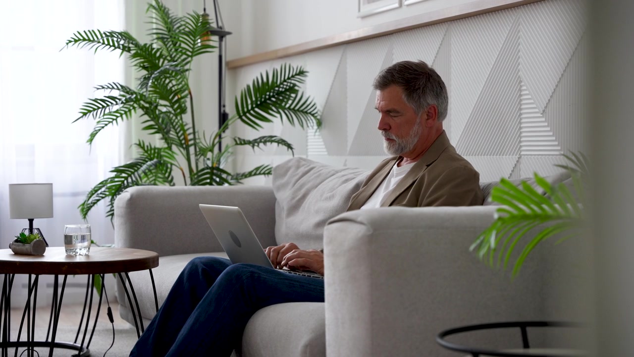 Mature Man Working on Laptop on Sofa in Modern Living Room