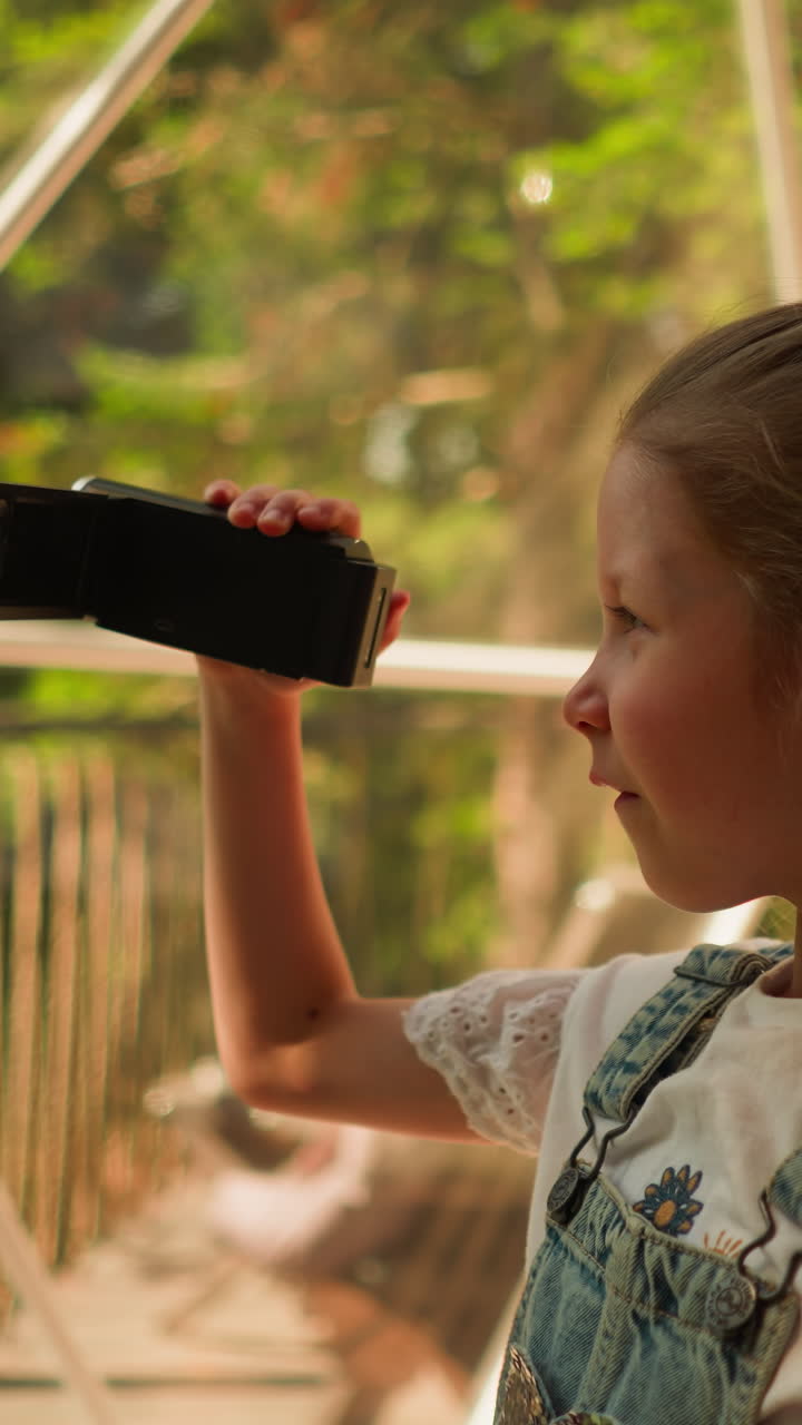niño graba tomas con cámara en glamping. niña concentrada graba video a través de una ventana panorámica en la terraza del hotel. niño toma tomas