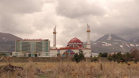 erzurum en turquía. 05.01.2021 el hospital de erzurum, al lado de una mezquita en el fondo es una montaña cubierta de nieve a finales de abril. turco: erzurum şehir hastanesi y darül fünun camii