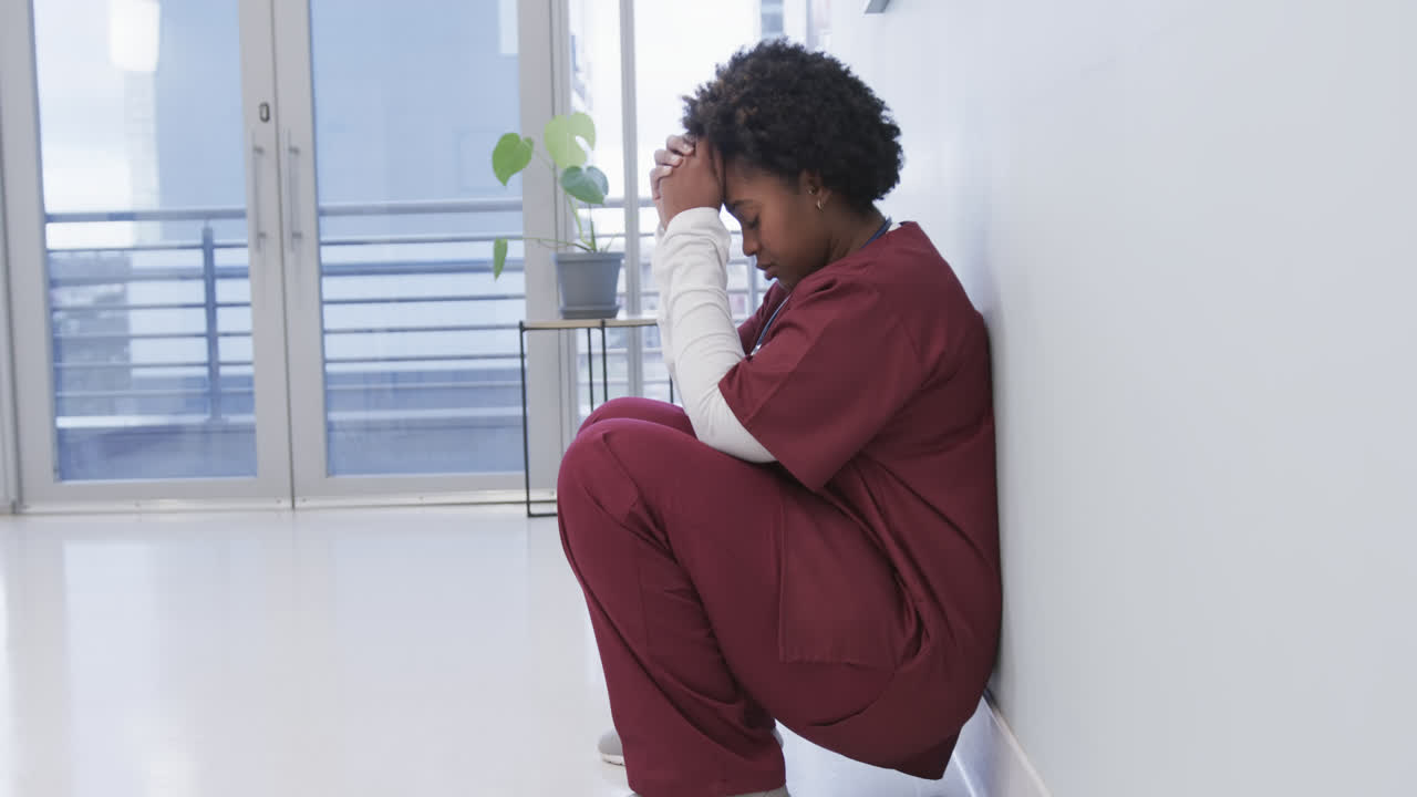 Médecin femme afro-américaine fatiguée accroupie dans un couloir d'hôpital, au ralenti