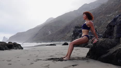 la cámara lenta revela la fuerza de una joven atleta mientras hace flexiones en una roca cerca del océano