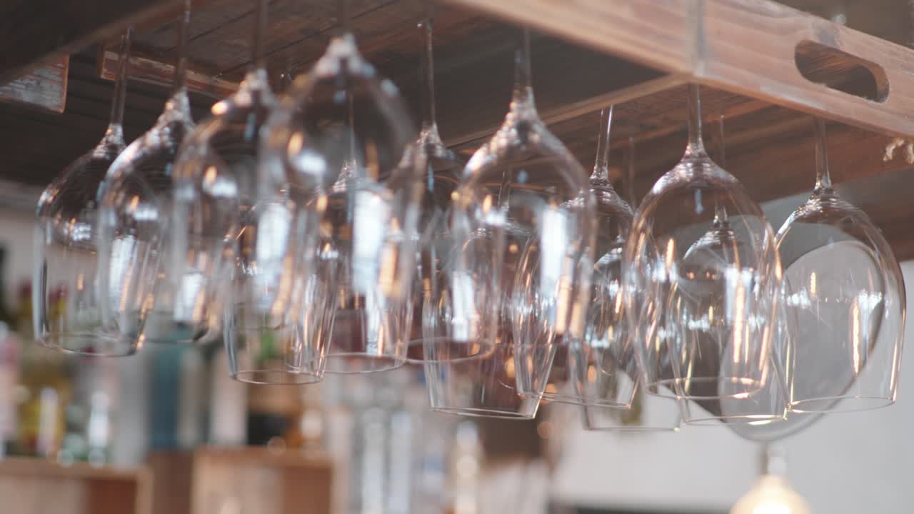 Copas de vino y vasos brillantes colgados boca abajo en una tabla de madera en un bar con un interior de madera vintage de fondo
