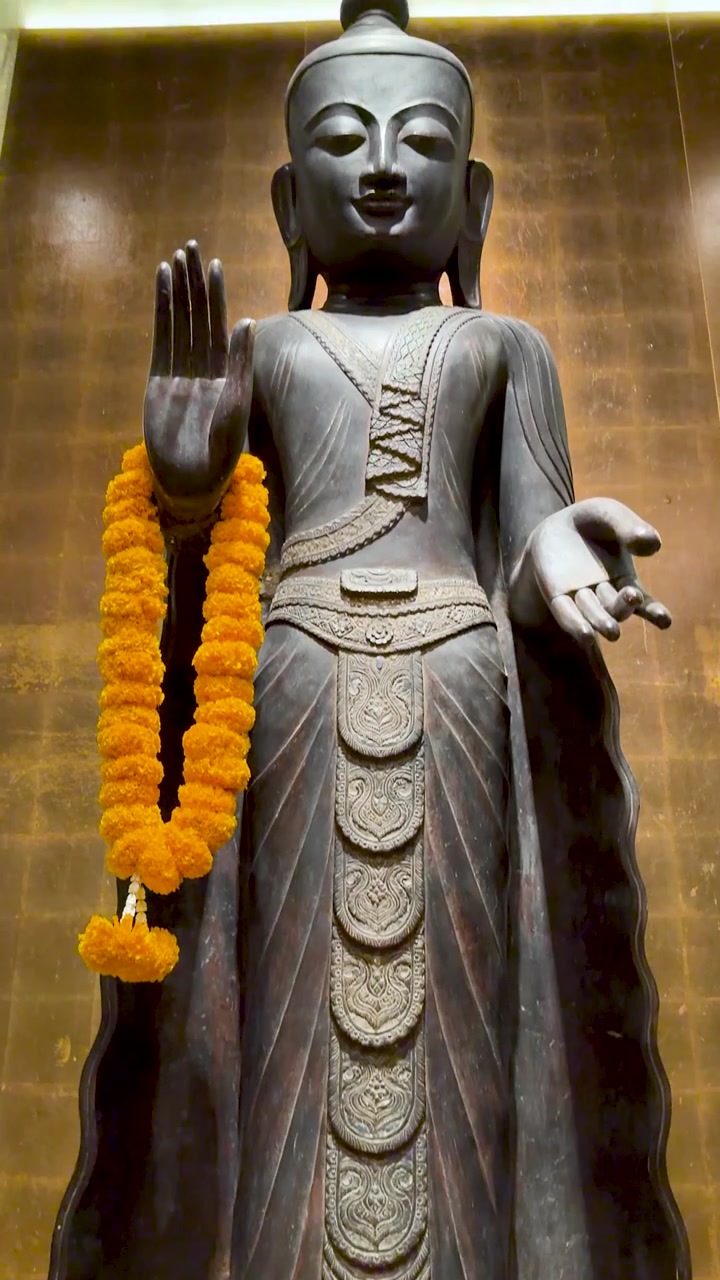 Lenta inclinazione verticale verso l'alto di una statua di Buddha in bronzo adornata con una ghirlanda di fiori di calendula gialla.