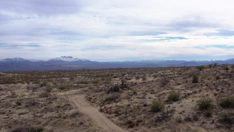 Retroceso-Aéreo-Para-Revelar-El-Suelo-Del-Desierto-De-Sonora-Bajo-Los-Cuatro-Picos-Nevados,-Scottsdale,-Arizona