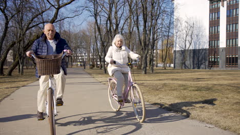 front view of a senior couple riding bikes in the park on a winter day while looking at camera