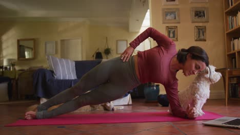 Caucasian-woman-exercising-with-her-pet-dog-using-laptop-at-home