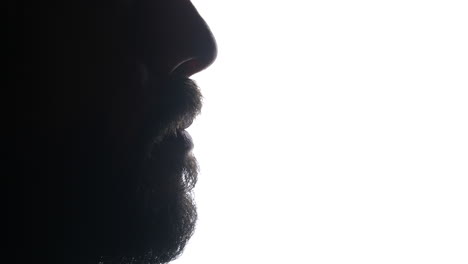 Man-putting-dental-oral-alignment-retainer-on-teeth,-silhouetted-against-illuminated-white-background