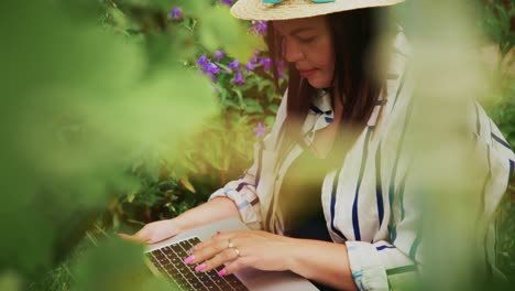 woman working on laptop in a lush garden surrounded by vibrant flowers and greenery