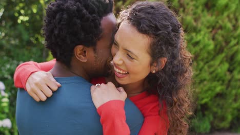 Happy-biracial-man-hugging-his-fiance-with-engagement-ring-on-hand-in-garden-in-sun