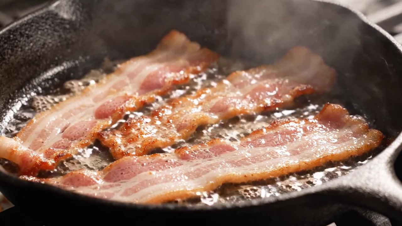Pancetta sfrigolante in una padella di ghisa: una vetrina culinaria di perfetta croccantezza, dal crudo alla deliziosa doratura.