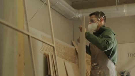 woodworker professional in mask and glasses checks wood raw, wooden plank, plywood panel